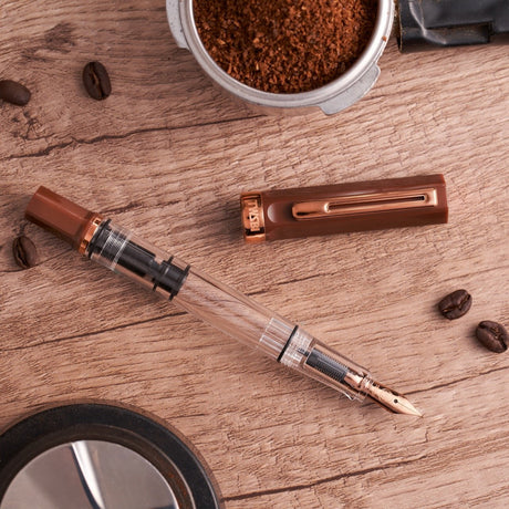 TWSBI Espresso Bronze Fountain pen on a wooden surface with coffee beans and a container of ground coffee.