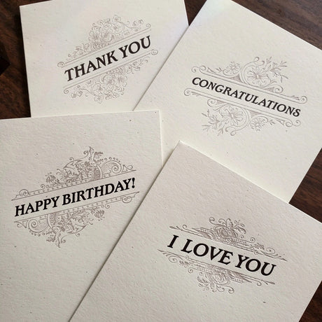 Four letterpress greeting cards with dark text and a flourish design on thick, off-white paper with messages Thank You, Congratulations, Happy Birthday!, and I Love You.