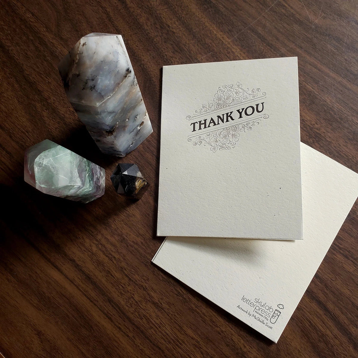 Letterpress greeting card with dark text 'Thank You' and floral flourish design on thick, off-white paper with Skylab Letterpress logo and artwork credit on back.