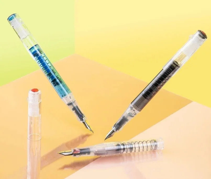 Set of three TWSBI Go Fountain pens with transparent bodies on a colorful background