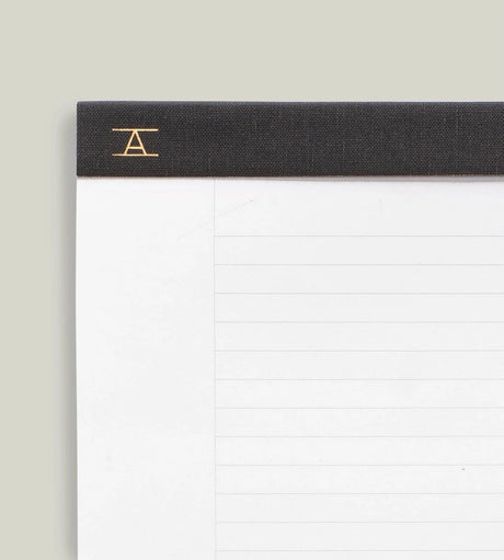 Closeup of Appointed Legal Pad bound with Charcoal Gray bookcloth and a gold foil Appointed logo in left corner, white paper with gray lined ruling.