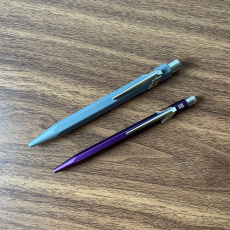 Caran d'Ache 849 Rollerball Pen Diagonally on table alongside 849 Ballpoint
