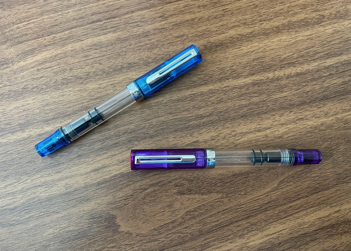TWSBI Transparent Blue ECO Fountain Pen next to Transparent Purple Fountain Pen