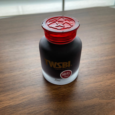 Bottle of TWSBI ink with red cap on a wooden surface