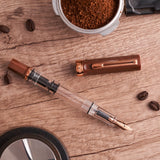 TWSBI Espresso Bronze Fountain pen on a wooden surface with coffee beans and a container of ground coffee.
