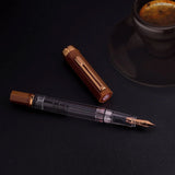 TWSBI Espresso Bronze Fountain pen on a dark surface with a cup of coffee in the background