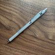 A silver TWSBI Precision Fixed Tip mechanical pencil with a textured grip and clip, resting diagonally on a brown wooden surface. 
