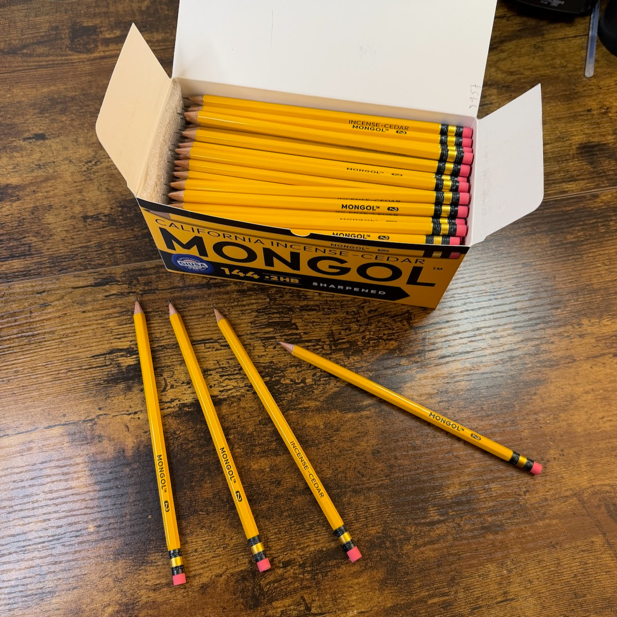 Mongol #2 Woodcase pencils displayed in a box of 144 pencils with three individual single pencils shown on a desk