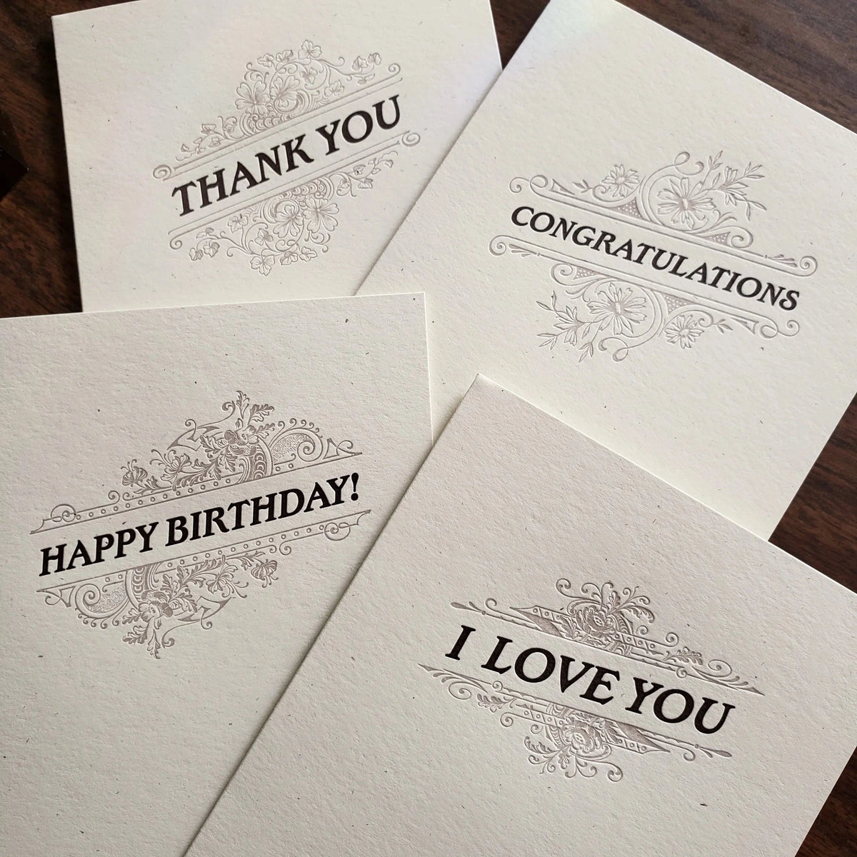 Four letterpress greeting cards with dark text and a flourish design on thick, off-white paper with messages Thank You, Congratulations, Happy Birthday!, and I Love You.