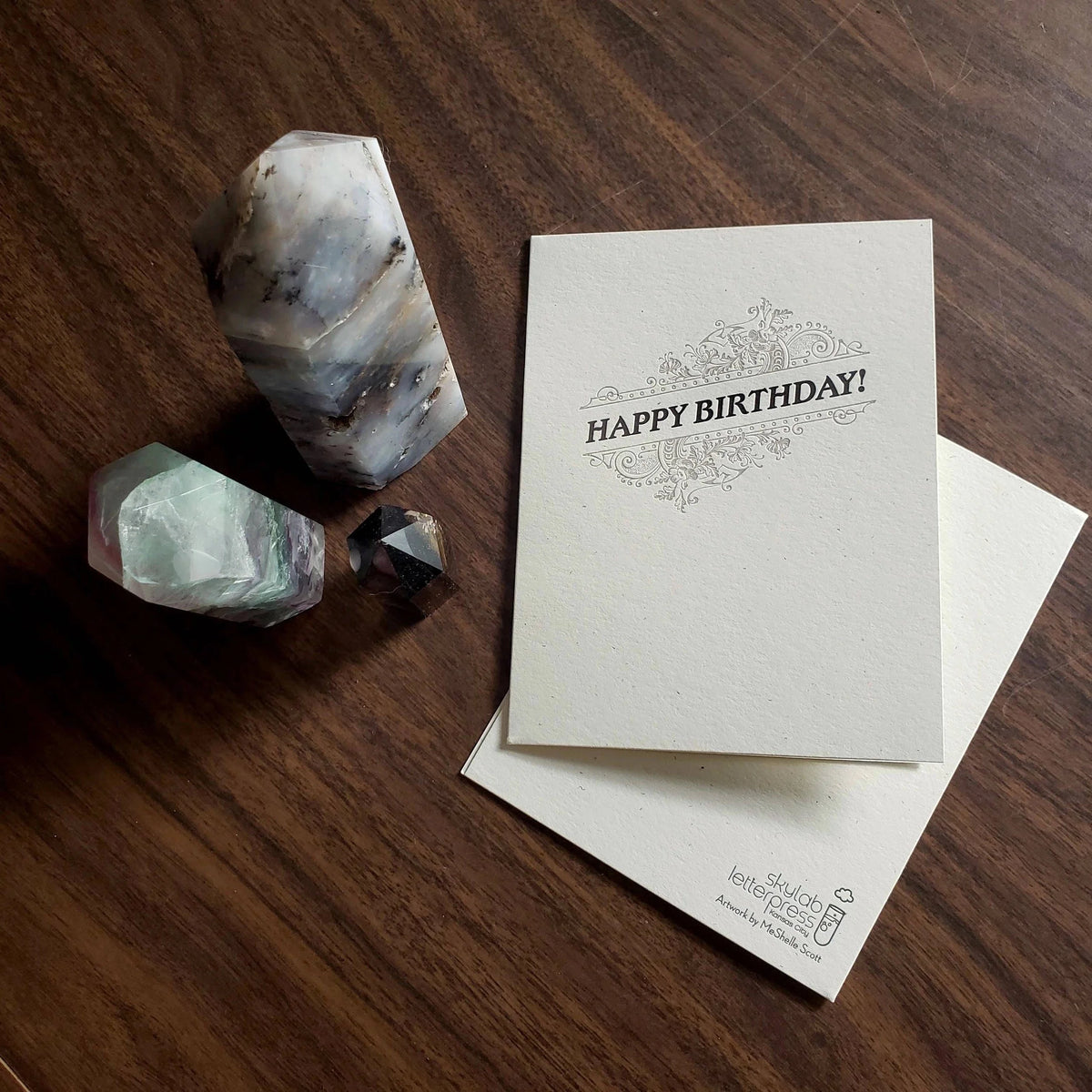 Letterpress greeting card with dark text 'Happy Birthday!' and flourish design on thick, off-white paper with Skylab Letterpress logo and artwork credit on back.