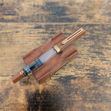 TWSBI Espresso Bronze fountain pen resting on a matching wooden pen stand over a rustic wood surface.