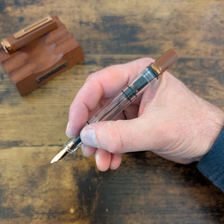 Hand holding a TWSBI Espresso Bronze fountain pen unposted with a wooden stand in the background