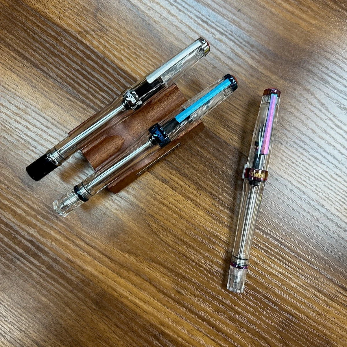 Three TWSBI Vac700R Fountain Pens in different finishes resting on a wood table